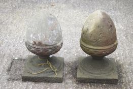 A pair of composite stone acorn finials, raised on a socle on a square plinth,