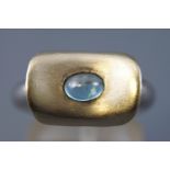 A yellow and white metal abstract ring set with an oval cabochon cut blue topaz.
