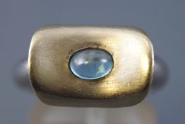 A yellow and white metal abstract ring set with an oval cabochon cut blue topaz.