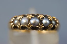 A yellow metal half hoop ring set with five graduated half pearls.