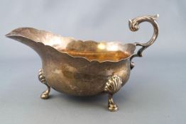A silver sauce boat of traditional form with cut card edge and flying scroll handle to a bellied