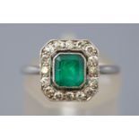 A white metal cluster ring. Principally set with a rectangular cut emerald estimated to weigh 0.