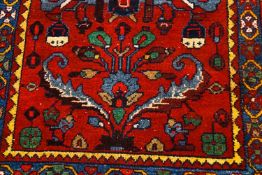 A rug with stylized flowers and leaves on a red ground within three borders,