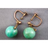 A yellow metal pair of drop earrings each having a circular polished green jade bead measuring