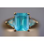 A yellow metal three stone ring set with a rectangular faceted cut blue topaz and flanked by a