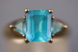 A yellow metal three stone ring set with a rectangular faceted cut blue topaz and flanked by a