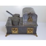 A Bing polished tinplate stove with two saucepans, on brass paw feet, 9.5" across