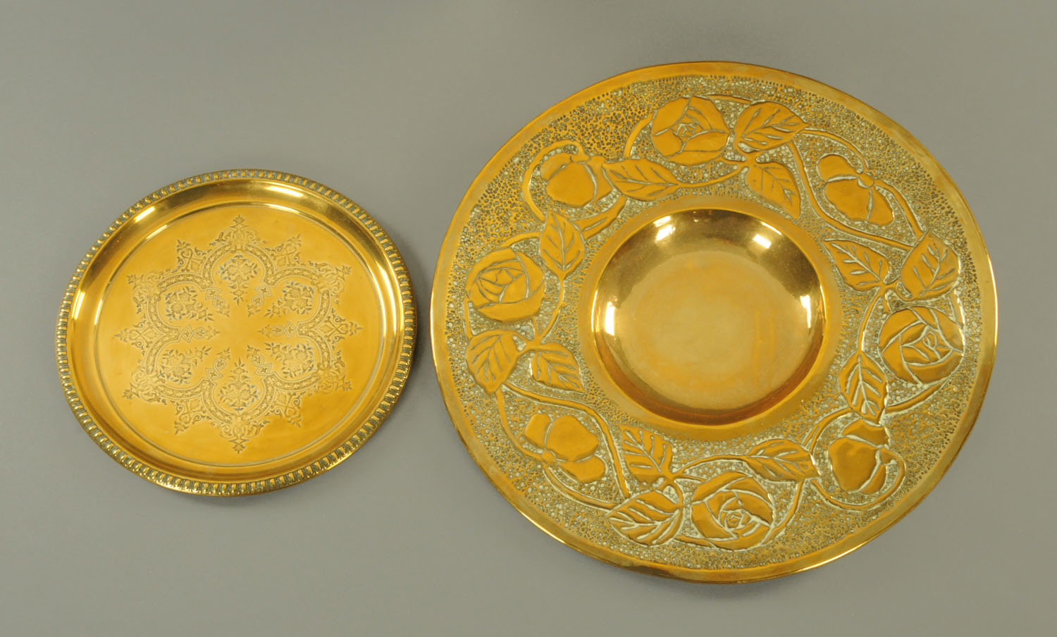 An Arts & Crafts embossed brass circular tray, diameter 46 cm, and another.