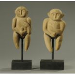 A pair of carved volcanic rock fertility figures, each raised on a rectangular stand.
