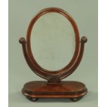 A Victorian mahogany framed dressing table mirror, oval with shaped base raised on bun feet,