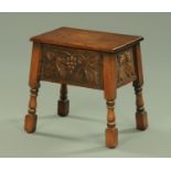 An oak stool, with hinged top, fruiting vine carved frieze and raised on tapered legs. Width 46 cm.