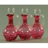 Three Victorian cranberry glass decanters, each of dimpled form. one stopper missing.
