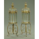 A pair of metal and glass lanterns, each with carrying handle and raised on a tripod stand,