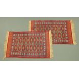 A pair of Indian woollen rugs, principal colours red, blue and orange, each with fringed ends,