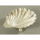 A Victorian silver scallop shaped dish, foliate engraved, raised on three ball feet, London 1891,