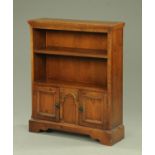 An oak open bookcase, with two shelves above cupboard doors and raised on bracket feet.