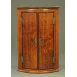A George III oak bow fronted corner cupboard,
