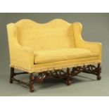 A Queen Anne style humpback settee, upholstered in yellow floral material with tasselled ends,