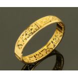An Egyptian gold metal hinged bangle, decorated with a scarab beetle, ankh's,