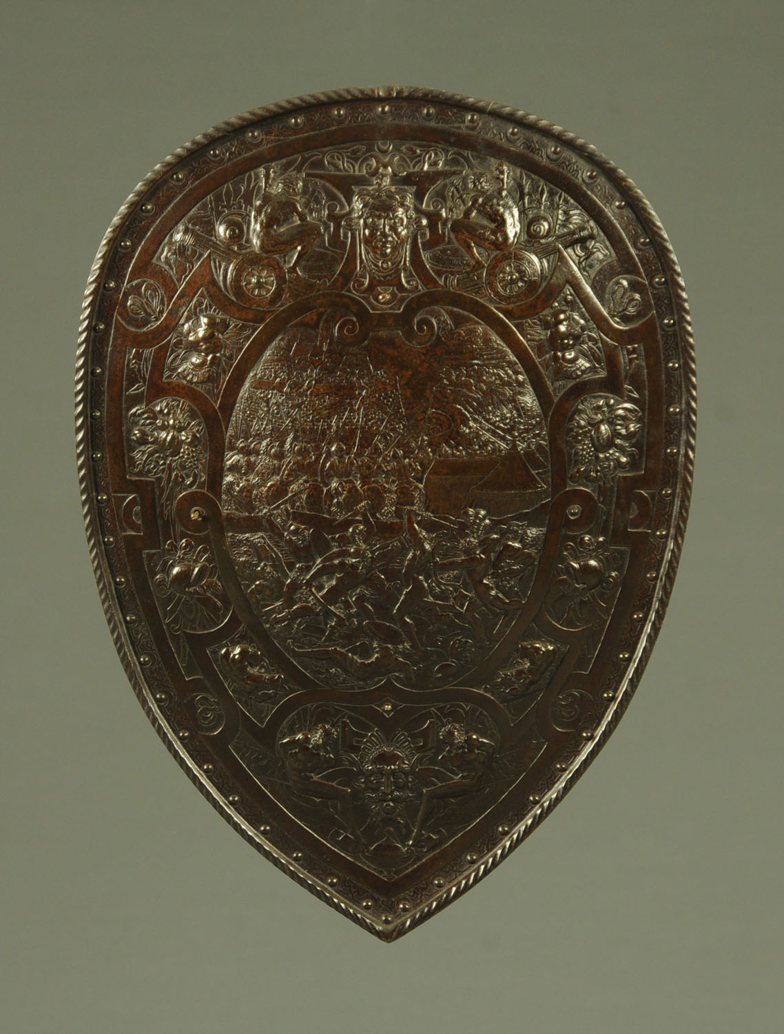 A bronzed metal shield, late 19th century, embossed with antiquarian battle scene to the centre,