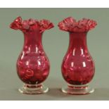 A pair of Victorian style cranberry glass dimpled vases, each with crimped rim and clear glass foot.
