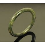A Chinese polished jade bangle, 20th century, of mottled green colour with natural inclusions,