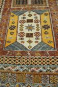 A Caucasian rug, the central panel set with repeating square medallions on a terracotta ground,