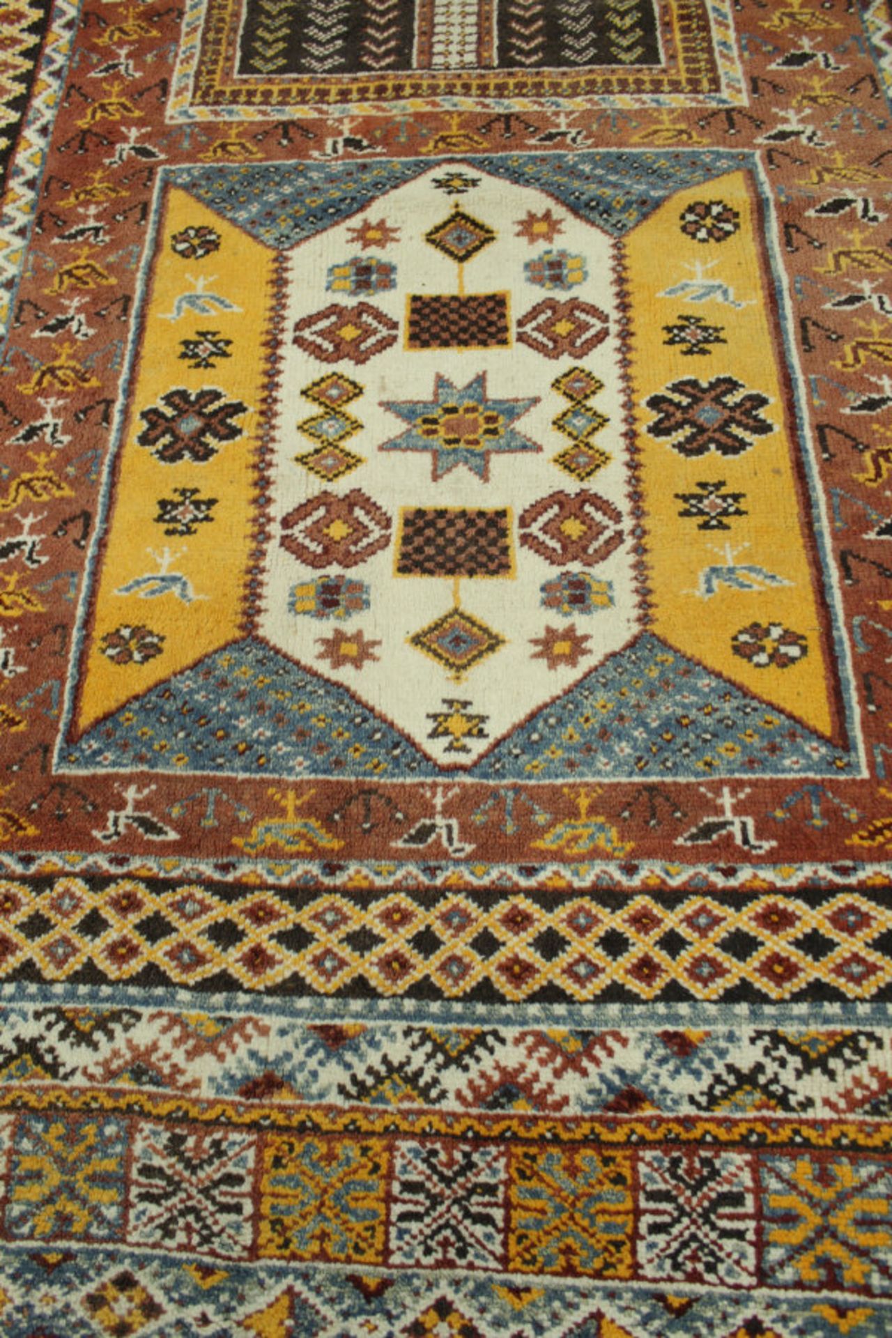 A Caucasian rug, the central panel set with repeating square medallions on a terracotta ground,