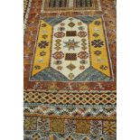 A Caucasian rug, the central panel set with repeating square medallions on a terracotta ground,