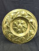 An Arts and Crafts brass charger with embossed scrolling foliate and flower head decoration