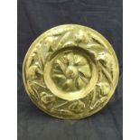 An Arts and Crafts brass charger with embossed scrolling foliate and flower head decoration