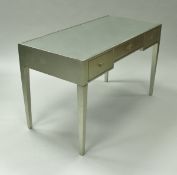 A modern silvered writing table, the mirrored top over three frieze drawers on square tapered legs,