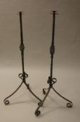 A pair of 20th century wrought iron floor standing candle holders on scrolling tripod supports