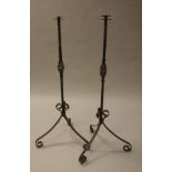 A pair of 20th century wrought iron floor standing candle holders on scrolling tripod supports