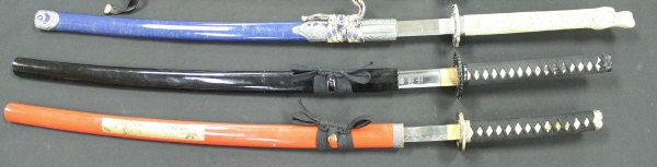 Three modern Japanese katanas with lacquered scabberds one with simulated ivory handle on a display