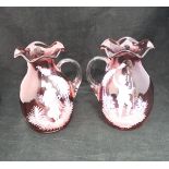 A pair of cranberry glass Mary Gregory style jugs with figural decoration