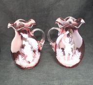 A pair of cranberry glass Mary Gregory style jugs with figural decoration