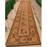 A Aubusson style runner the central panel set with repeating floral set tiles on a cream ground