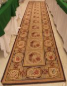 A Aubusson style runner the central panel set with repeating floral set tiles on a cream ground