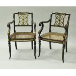 A pair of ebonised and gilt decorated open scroll arm elbow chairs with cane seats in the Regency