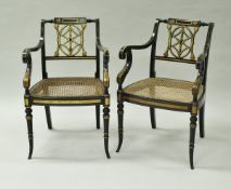 A pair of ebonised and gilt decorated open scroll arm elbow chairs with cane seats in the Regency