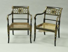 A pair of ebonised and gilt decorated open scroll arm elbow chairs with cane seats in the Regency