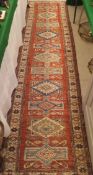 A Caucasion carpet the central panel set with repeating geometric medallions on a red ground within