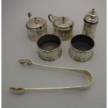 A George V silver cruet of faceted form comprising two open salts, two lidded mustards,
