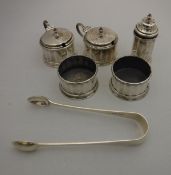 A George V silver cruet of faceted form comprising two open salts, two lidded mustards,