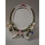 A Dresden porcelain framed mirror with laurel wreath and cherubic relief work decoration bearing