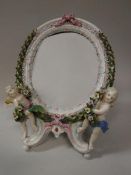 A Dresden porcelain framed mirror with laurel wreath and cherubic relief work decoration bearing