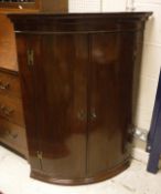 A George III mahogany bow fronted hanging corner cupboard,