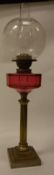 A Victorian brass column oil lamp with cranberry glass faceted reservoir and acid etched globe
