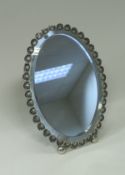 An Italian white metal framed oval easel back mirror with scallop shell edge and bun feet